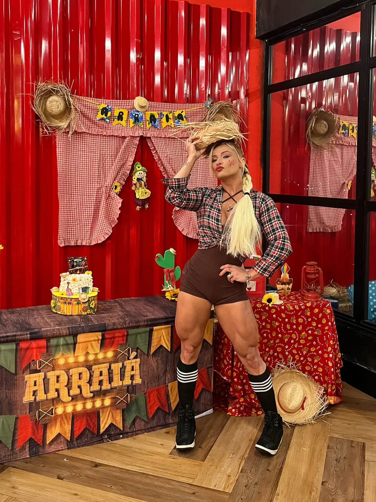Evelyn Soares vestida de caipira em um cenário de arraiá, com chapéu de palha e camisa xadrez
