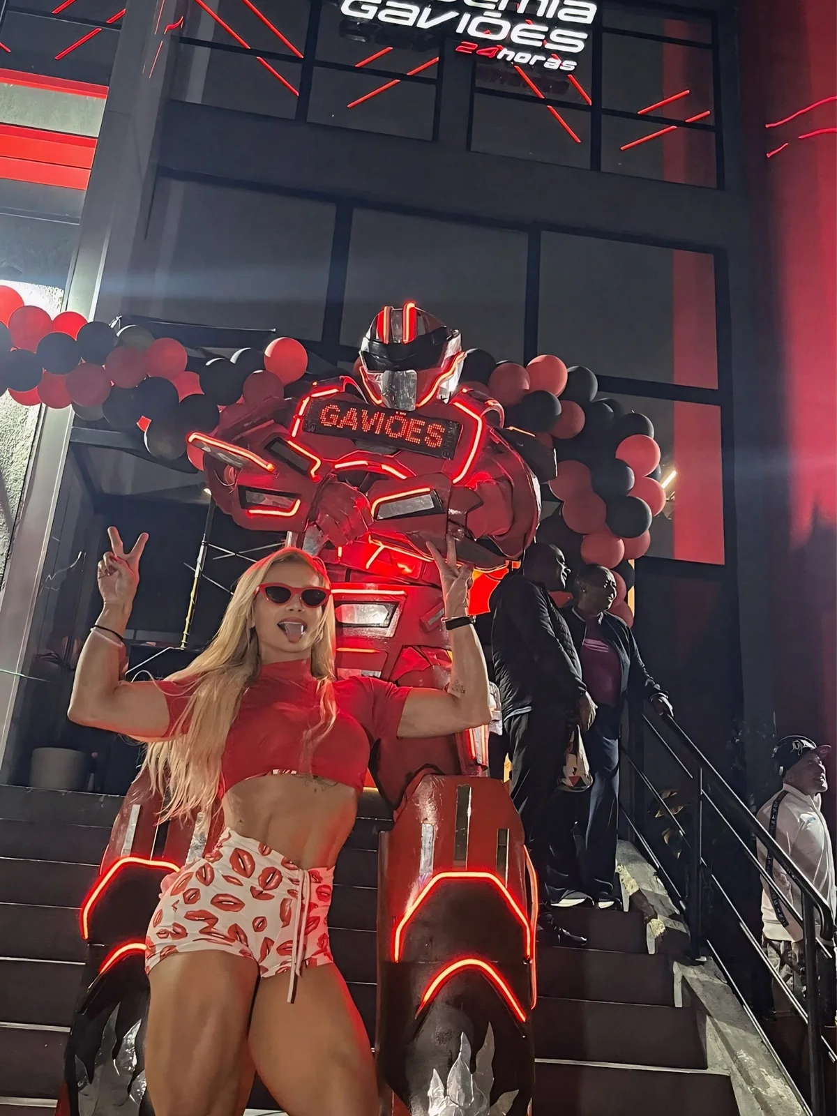 Evelyn Soares de top vermelho ao lado do robô gigante de luzes da Academia Gaviões