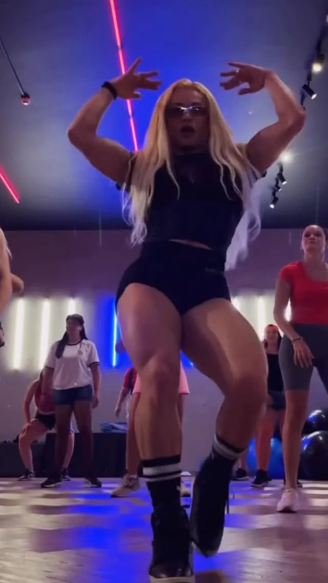 Evelyn Soares dançando de braços erguidos em um aulão de funk sob luzes azuis